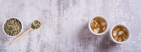 Iced green japanese hojicha tea in cups and leaves in a bowl top view web bannerの写真素材