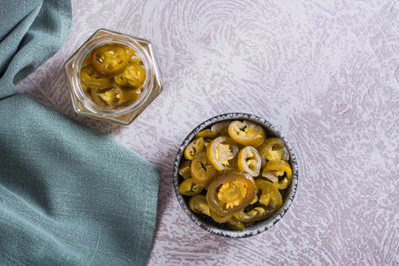Sliced pickled jalapeno peppers in bowl and glass jar on table top viewの写真素材