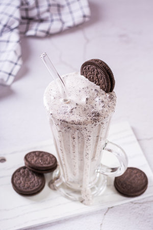 Homemade smoothie with cream and whipped chocolate chip cookies in a glass with a straw vertical viewの写真素材