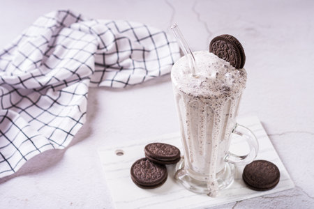 Homemade smoothie with cream and whipped chocolate chip cookies in a glass with a strawの写真素材
