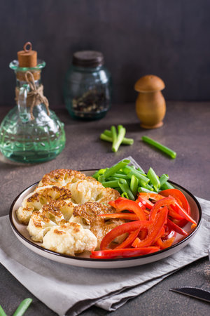 Cauliflower steaks with vegetables and herbs on a plate on the table vertical viewの写真素材