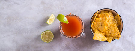 Michelagua mocktail with tomato juice and lime juice in a glass and nachos in a bowl top view web bannerの写真素材