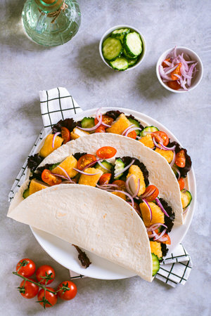 Tacos with chicken nuggets, cucumber, tomato, onion and lettuce on a plate top and vertical view