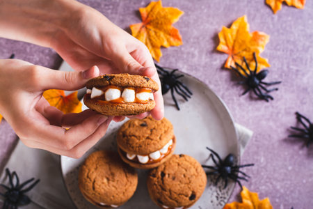 Close-up gingerbread cookies with marshmallow teeth in children's hands for halloween top viewの写真素材