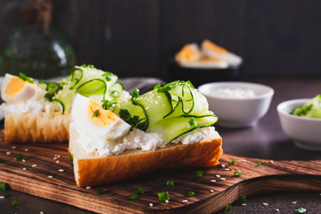 Appetizing sandwich with ricotta, cucumber slices, boiled egg and sesame seeds on a boardの写真素材