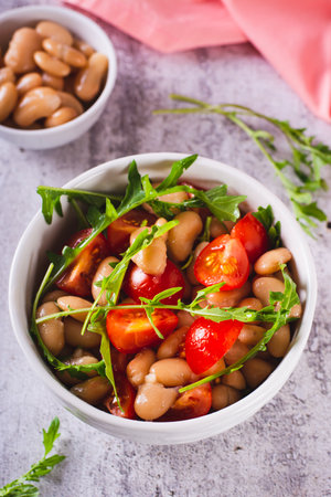 Homemade salad of white beans, cherry tomatoes and arugula in a bowl vertical viewの写真素材