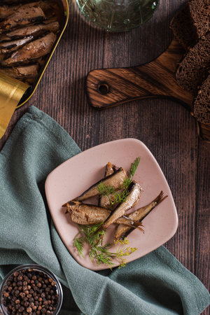 Canned smoked sprats in oil and on a plate on the table top and vertical view