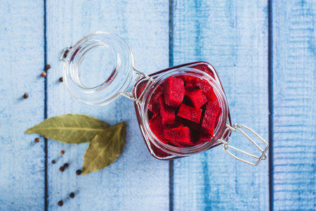 Close up of pieces of fermented beets in a jar and spices on the table top view