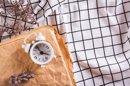 Change to winter time. Alarm clock on an old book on a checkered crumpled fabric top viewの写真素材