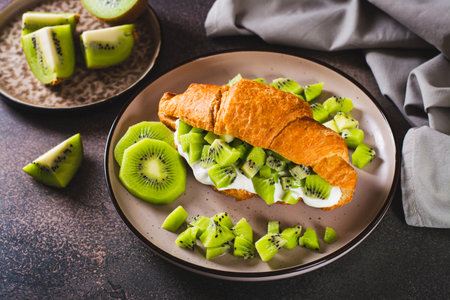 Croissant sandwich kiwi fruit and yogurt on a plate on the tableの写真素材