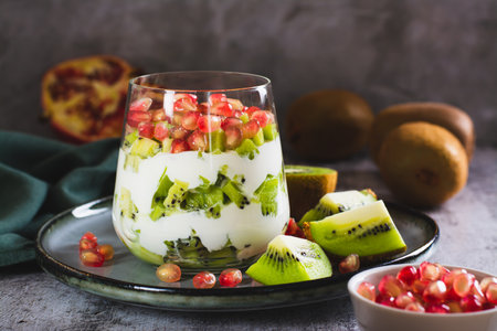 Fresh Greek yogurt with kiwi pieces and pomegranate seeds in a glass on the tableの写真素材