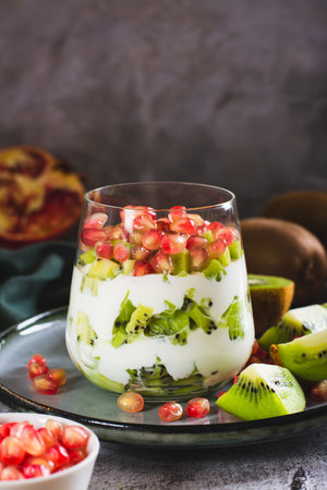 Fresh Greek yogurt with kiwi pieces and pomegranate seeds in a glass on the table vertical viewの写真素材