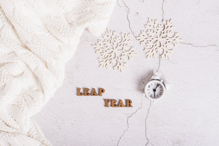 Leap year concept, calendar, alarm clock, sweater and snowflakes on a light top viewの写真素材