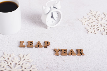Leap year concept, text from wooden letters, alarm clock, coffee and snowflakes on light