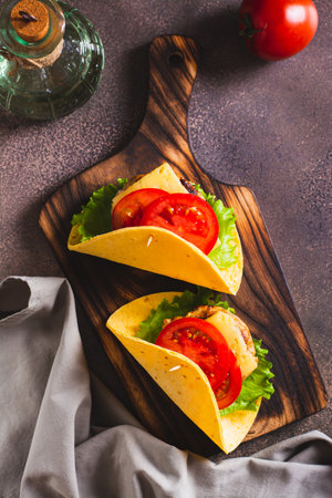 Taco burger in tortilla with cutlet, cheese and tomatoes on a board top and vertical viewの写真素材