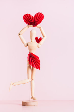 Wooden man decorated with paper red hearts and leaves on a pink background vertical viewの写真素材