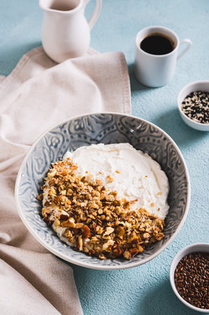 Granola with nuts in a bowl with classic yogurt for healthy eating on the table vertical view