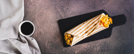 Appetizing burrito in a tortilla made of chicken, corn and peppers on a board top view web bannerの写真素材