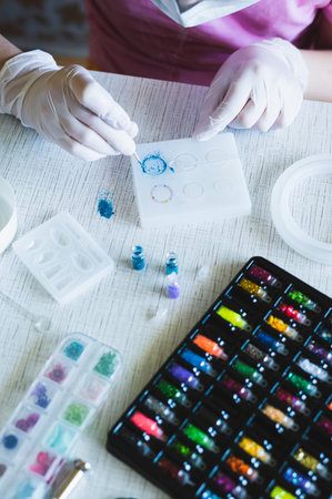 Children's hands in gloves fill an epoxy resin ring mold with decorative sparkles vertical view