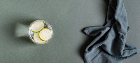 Refreshing water with lime slices in a glass and a cloth on a green background top view web banner