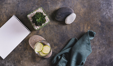 Clean water with lime slices in a glass on a stone, notebook and succulent on the table top view