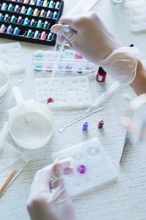 Children's hands in gloves fill a crystal mold with epoxy resin from a pipette vertical view