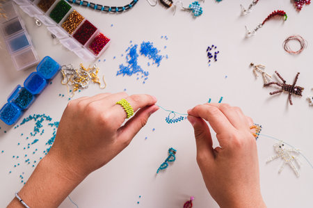 A girl's hands weave a beaded ring on a wire above a work table with finished jewelry