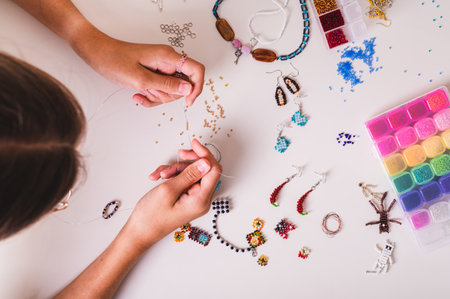 Hands of a girl weaving a beaded jewelry on a work table with beading supplies top view