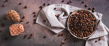 Unshelled pine nuts on a tray and pine cones on a table top view web banner