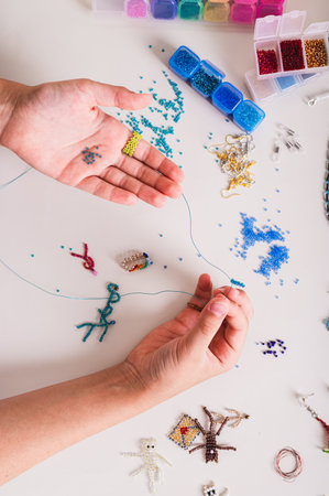Hands of a girl weaving a beaded jewelry on a work table with beading supplies vertical view