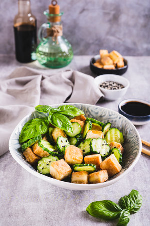 Fresh cucumber and fried tofu salad with basil leaves in bowl on table vertical viewの写真素材