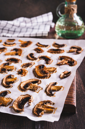 Baked spicy mushroom chips on paper on a wooden board vertical view