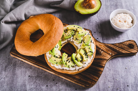 Bagel burger with ricotta, avocado and sesame seeds on a board on a tableの写真素材