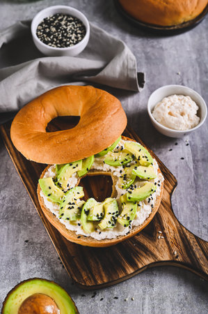 Bagel burger with ricotta, avocado and sesame seeds on a board on a table vertical view