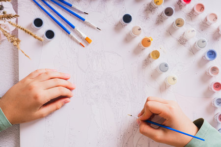 A girl paints a picture by numbers with a brush using a paint set top viewの写真素材