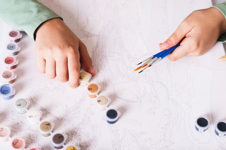 Girl's hands holding brushes and paints for painting by numbers