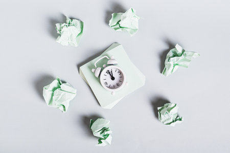 Burnout breaks concept. Alarm clock among crumpled papers on a desk top view