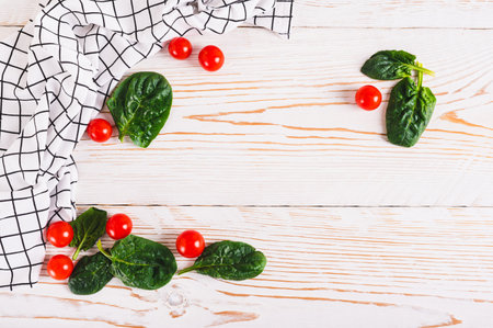 Spinach leaves, cherry tomatoes and fabric on white wooden background top viewの写真素材