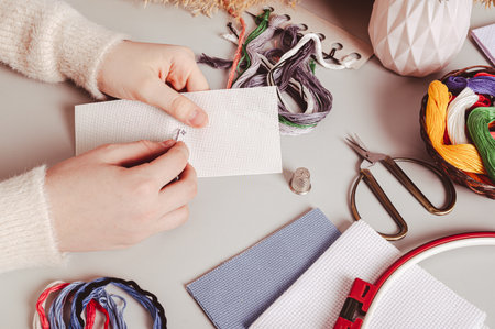 Female hands cross stitching on canvas on table among equipment
