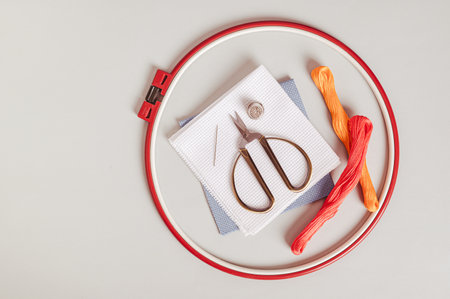 Close up of anvas, embroidery floss, scissors, needle, thimble and cross stitch hoop top view
