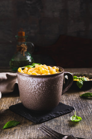 Pasta with gratified cheese baked in a mug and basil leaves on the table vertical viewの写真素材