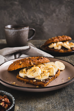 Sweet sandwich with chocolate butter, banana and nuts on a plate on the table vertical viewの写真素材