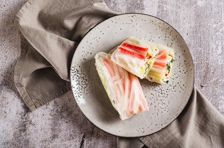 Close up of spring rolls in rice paper with crab sticks, cucumber, greens and sauce on top viewの写真素材
