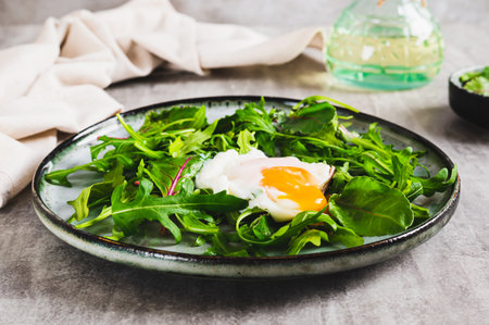 Poached egg in arugula and chard leaves on a plate on a tableの写真素材