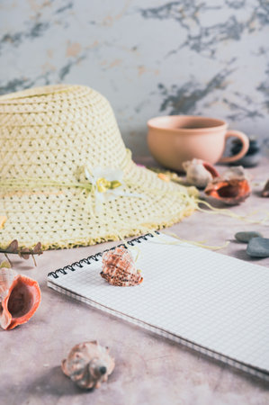 Travel planning notebook, hat, seashells and cup of coffee on table vertical viewの写真素材