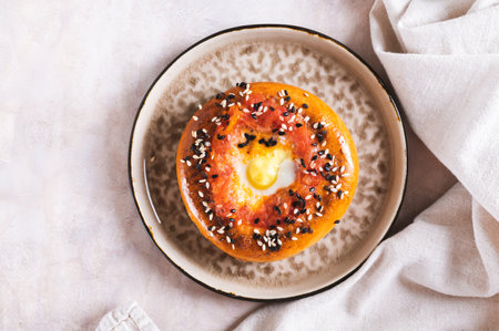 Close up of baked bagel with tomato and quail egg on a plate on the table top viewの写真素材