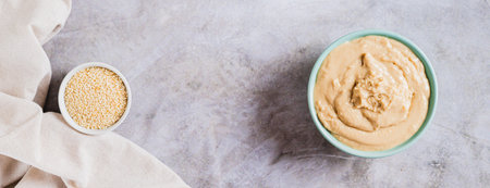Homemade sesame tahini in bowl on gray table top view web banner