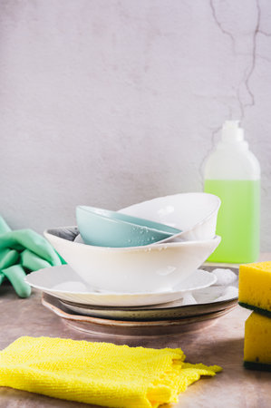 Stack of plates in foam, cloth, sponges, gloves and detergent on table vertical viewの写真素材