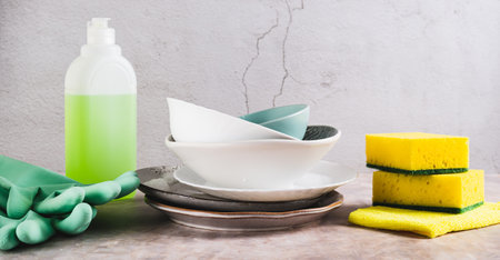 Stack of plates in foam, cloth, sponges, gloves and detergent on table web banner