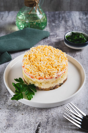 Classic mimosa salad with canned fish and vegetables on a plate on the table vertical viewの写真素材